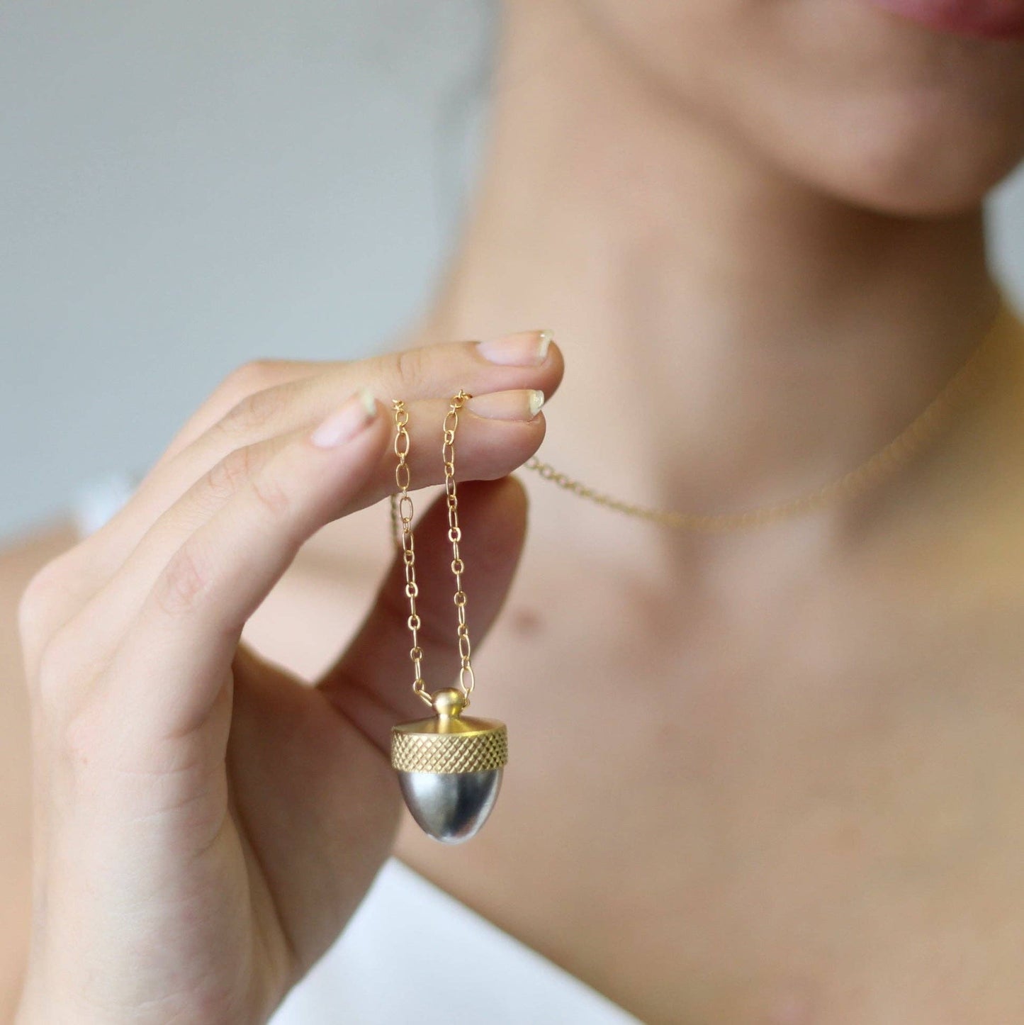 image of a lady holding up the silver acorn necklace with gold top and gold chain