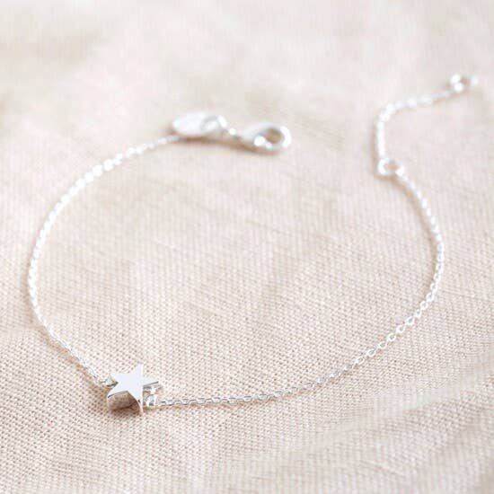 Silver bracelet with star charm on a beige fabric background