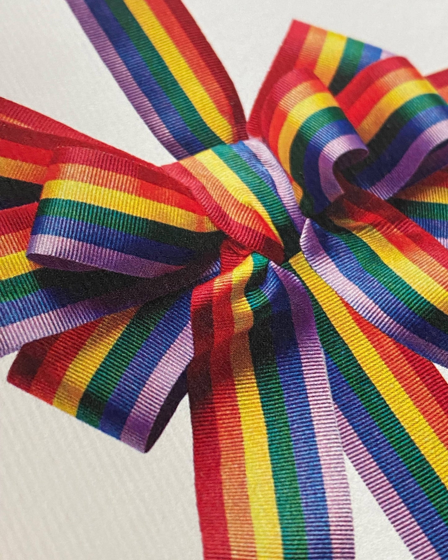 Greetings Card with a Multicoloured Ribbon looking bow on the front. In Pride colours purple blue green yellow orange and red. Looks like real material but it is an image White Background. White Envelope.