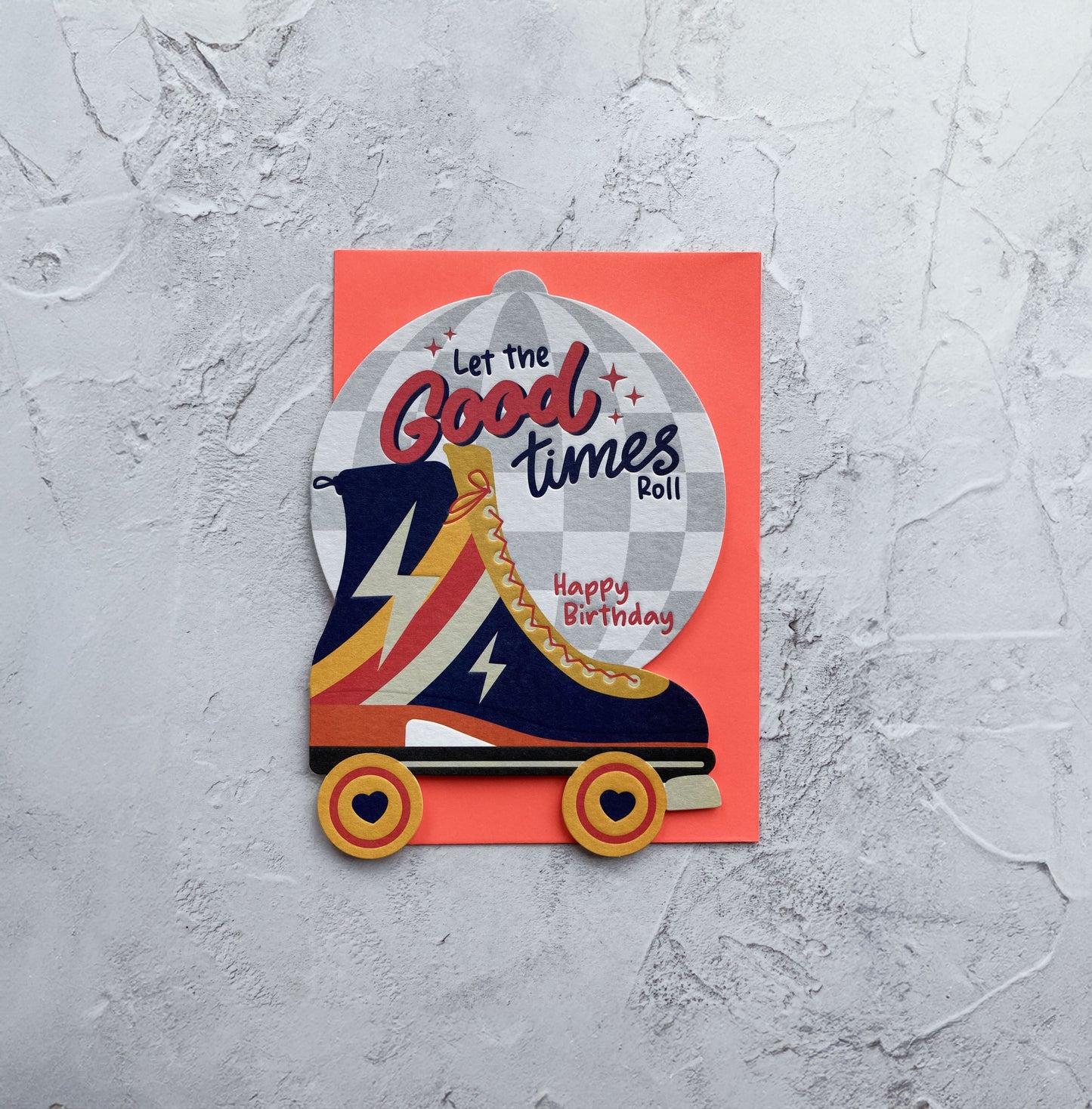 Roller derby boot with 'Let the Good Times Roll' text on a red card against a gray textured background