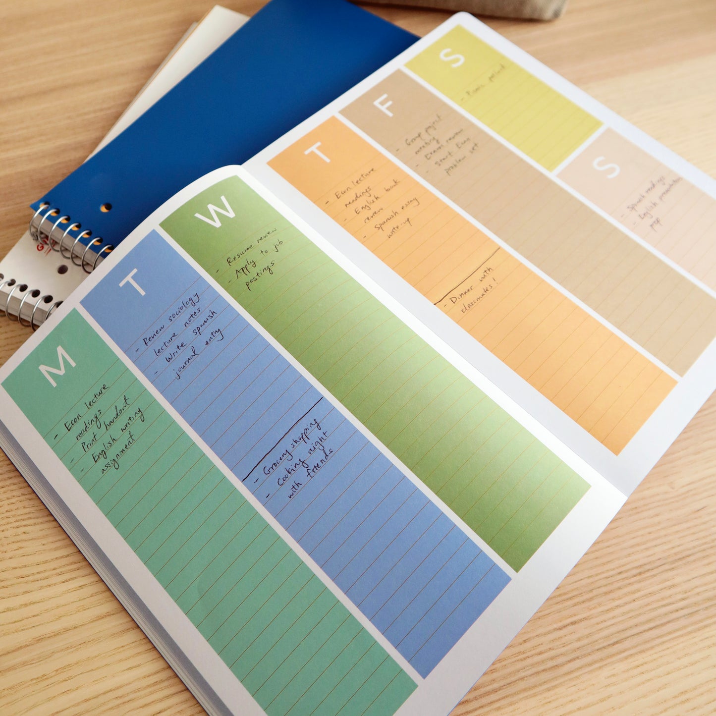 image of a page from the weekly planner. there are 6 different coloured verticle columns with the first letter of each d . the last column is split into the weekend. the week is across 2 pages
