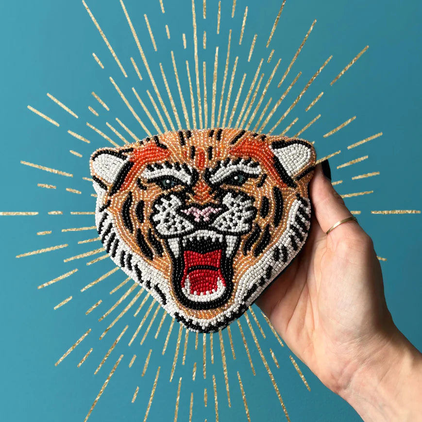 Hand holding a beaded tiger head purse against a blue background with gold accents