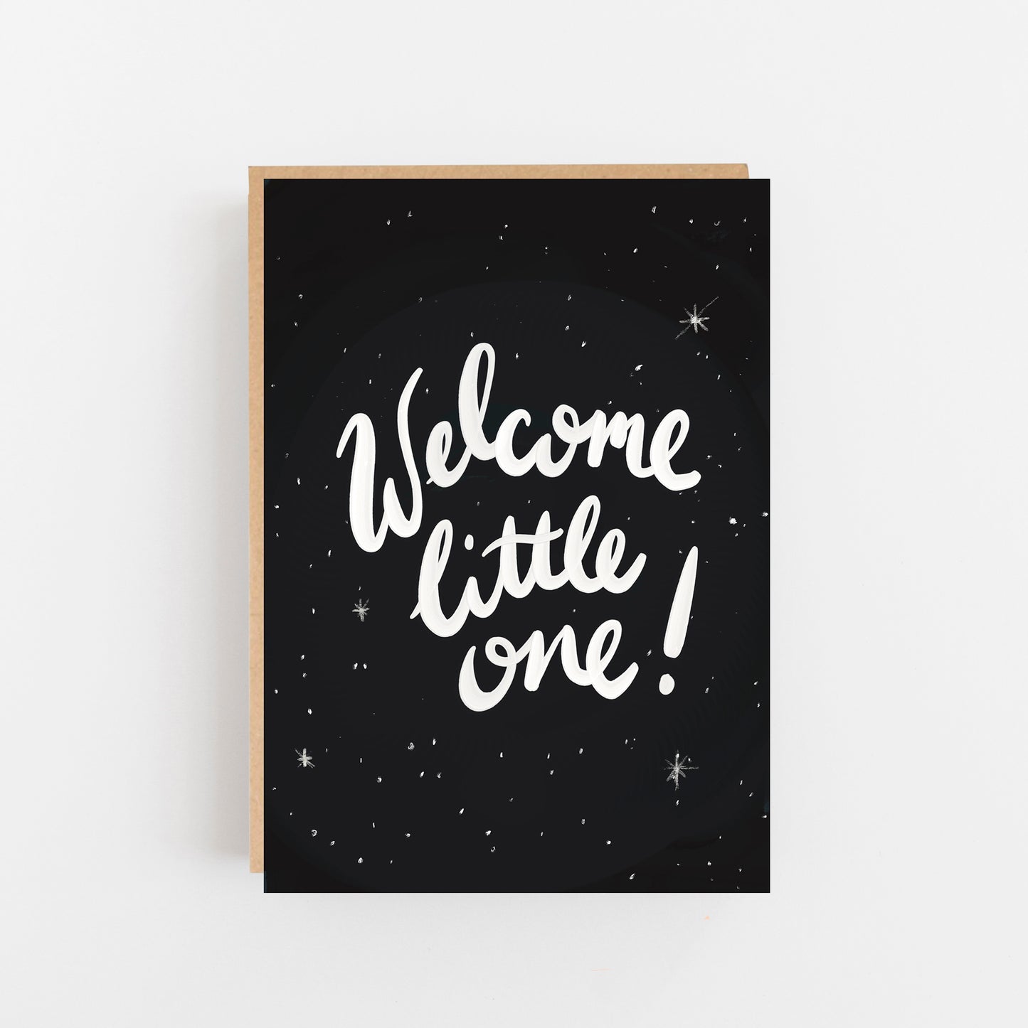 Greeting Card with Black background with wite small spots and stars. The words Welcome little one! written in white on the centre of the card. Brown Kraft Envelope