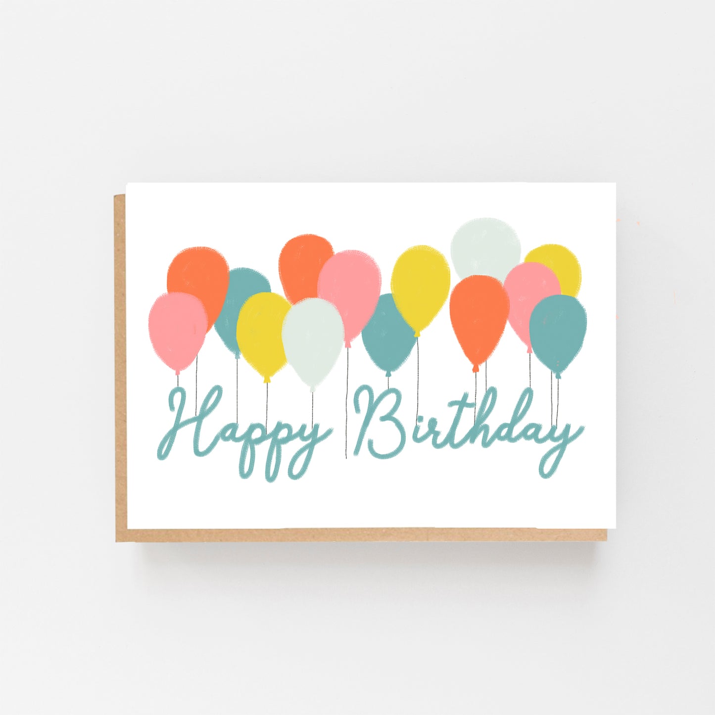 Greetings card in landscape.White Background with a row of pastel coloured balloons all across the centre of the card. With the words Happy Birthday in pale blue italics. Brown Kraft Envelope.