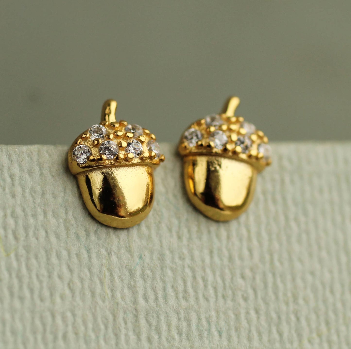 close up image of a pair of brass acorn shaped earrings with crystal tops