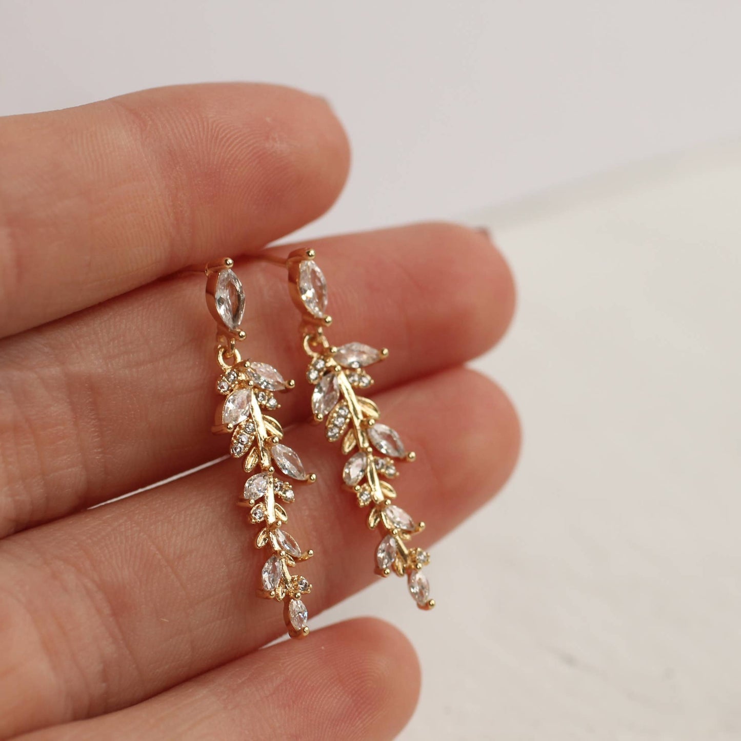 close up image showing a pair of the long crystal drop earrings being held against a ladies fingers