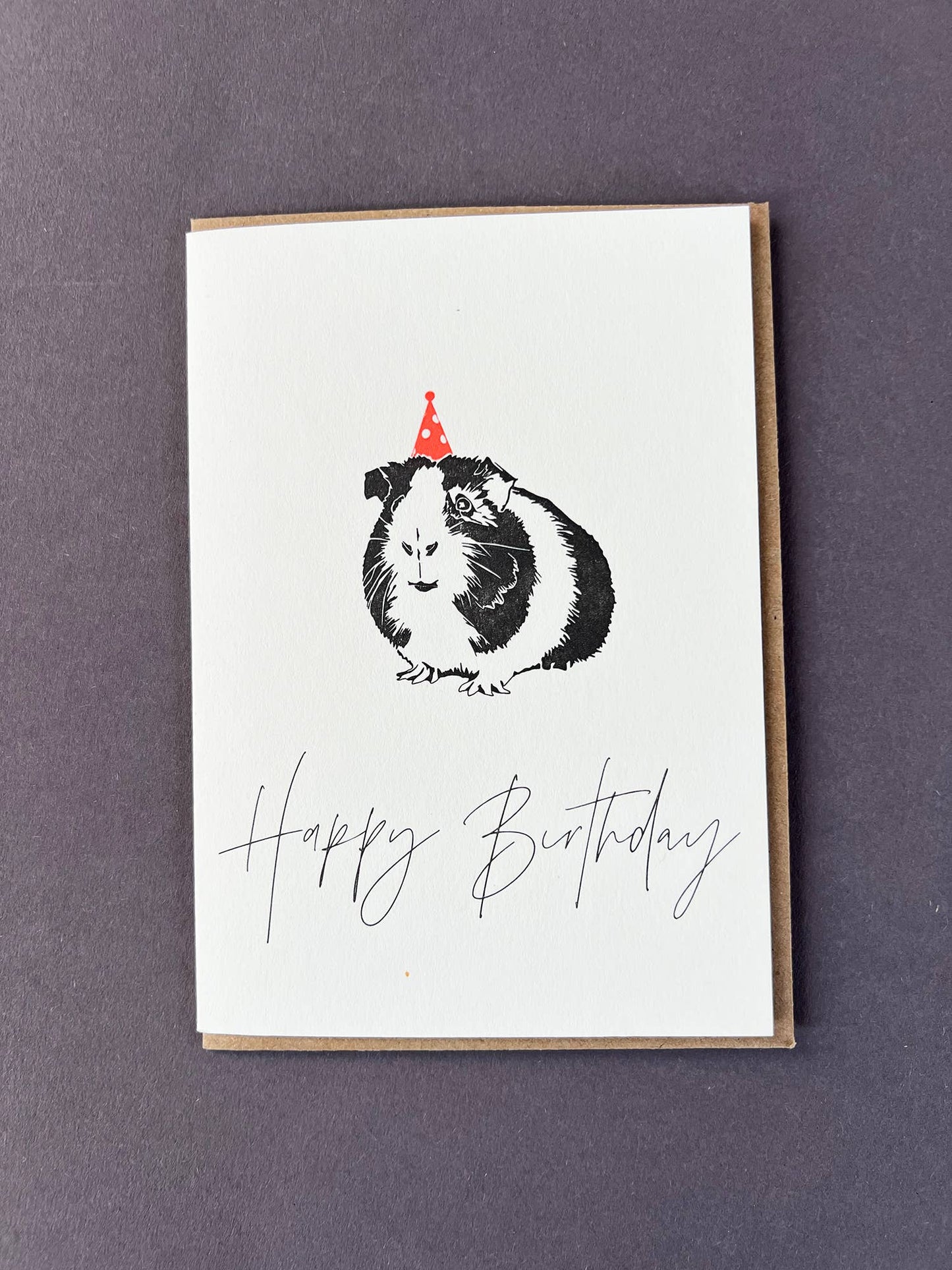 Greeting card with a guinea pig wearing a party hat and 'Happy Birthday' text on a purple background