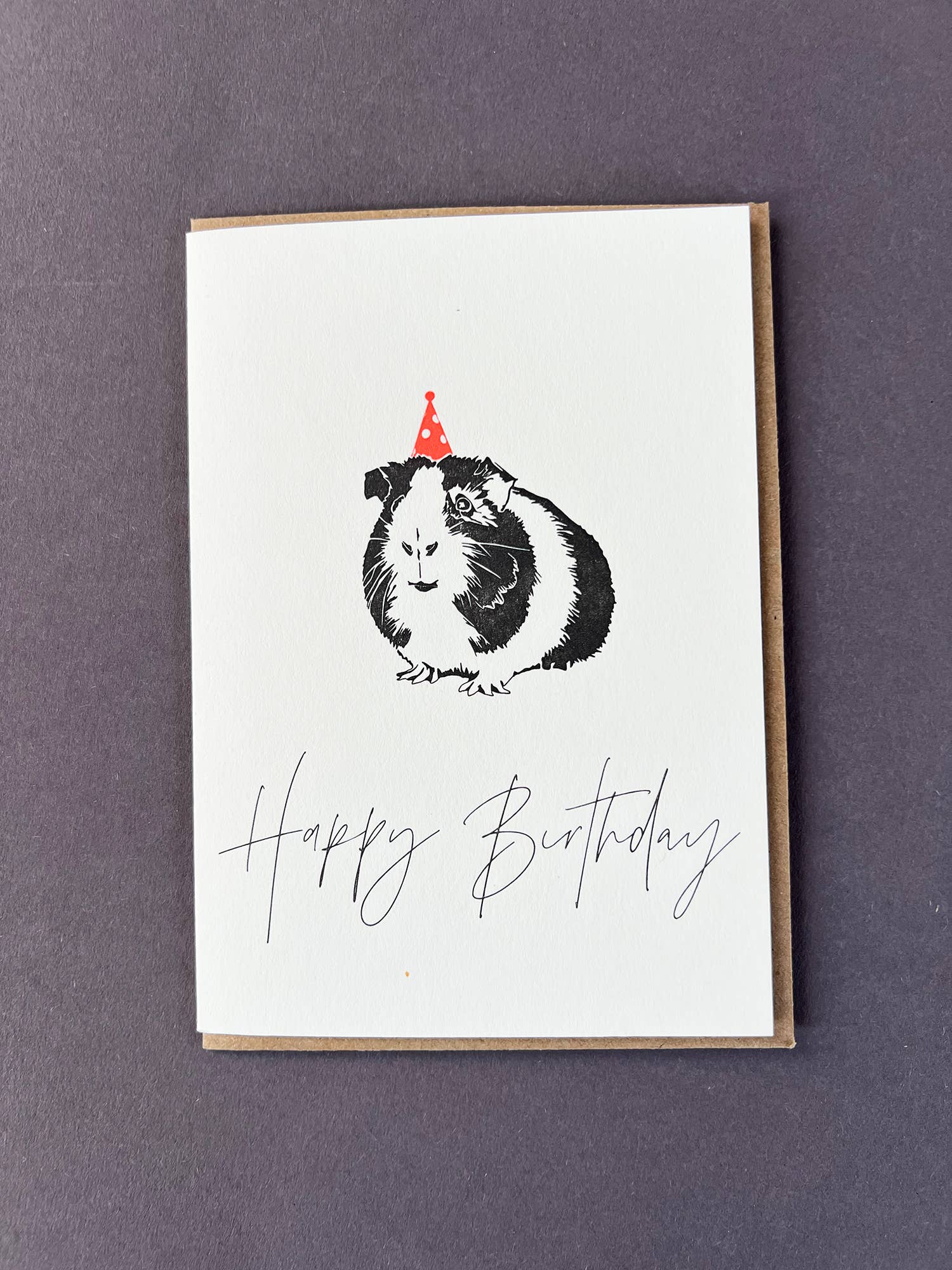 Greeting card with a guinea pig wearing a party hat and 'Happy Birthday' text on a purple background