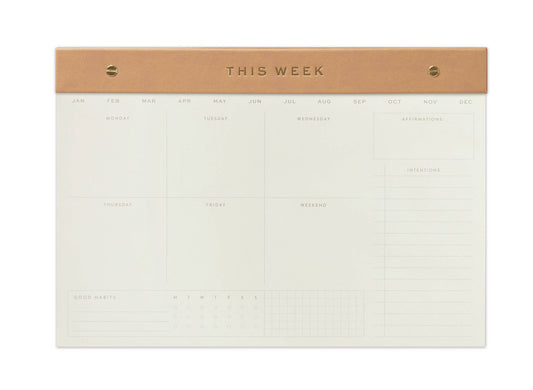 image of a desk top pad. At the top of the pad is a faux beige leather strip that holds the pad together.  the word This week is embossed in gold in the centre of this strip. the months of the year are printed horizontally across the top of the page. The days of the week are each printed in a sperate box with space for writing. at the bottom of the page is a full undated month 
 & space for intentions. the paper is cream and the wording is all gold foil embossed.