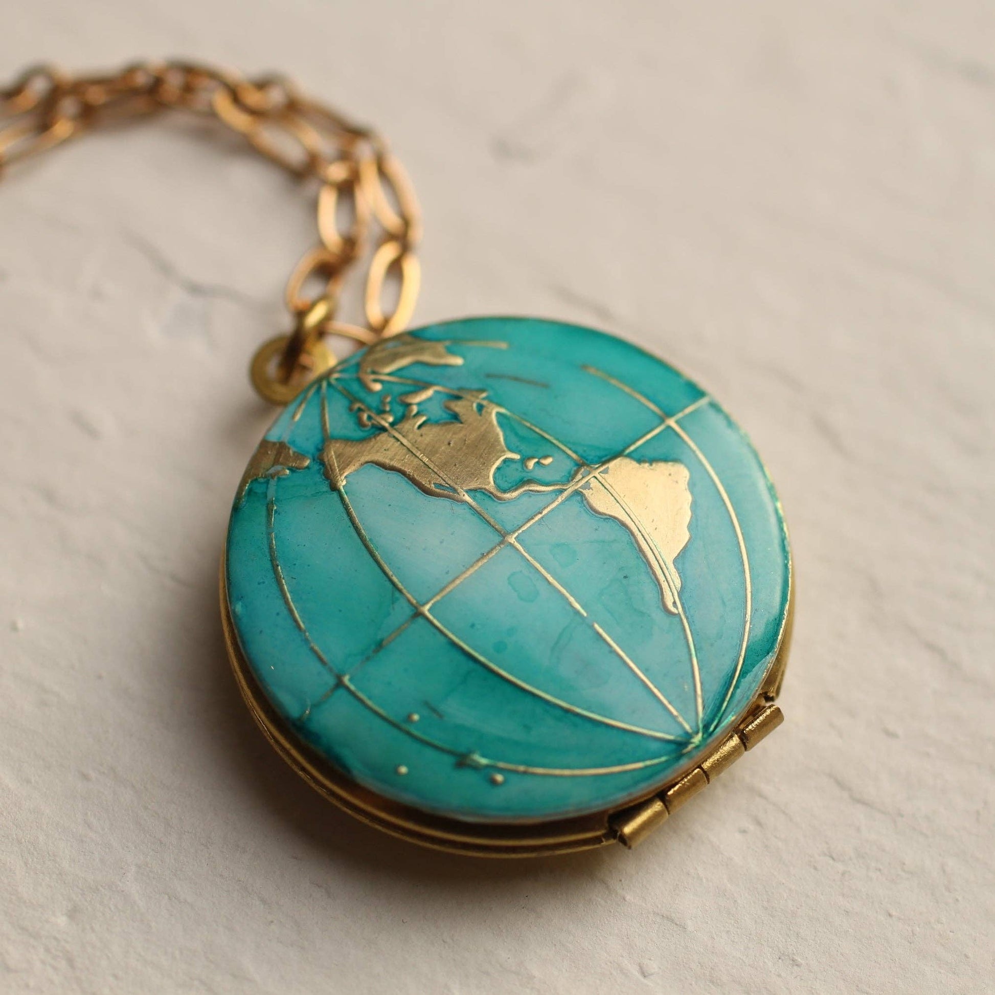 close up image of the turquoise world map locket with gold chain.