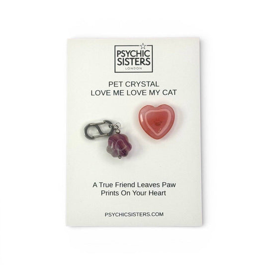 A pinkish-red heart-shaped pet crystal charm and a purple paw-print charm displayed on a white card from Psychic Sisters London.