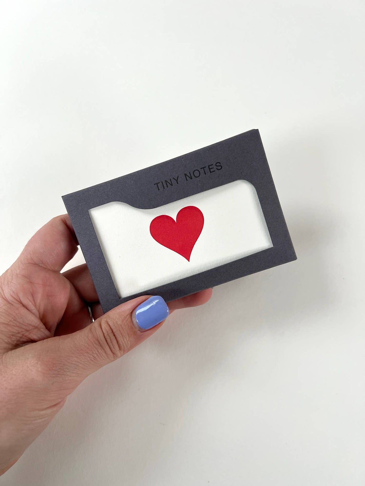 Hand holding a small black box with a red heart design on a white background