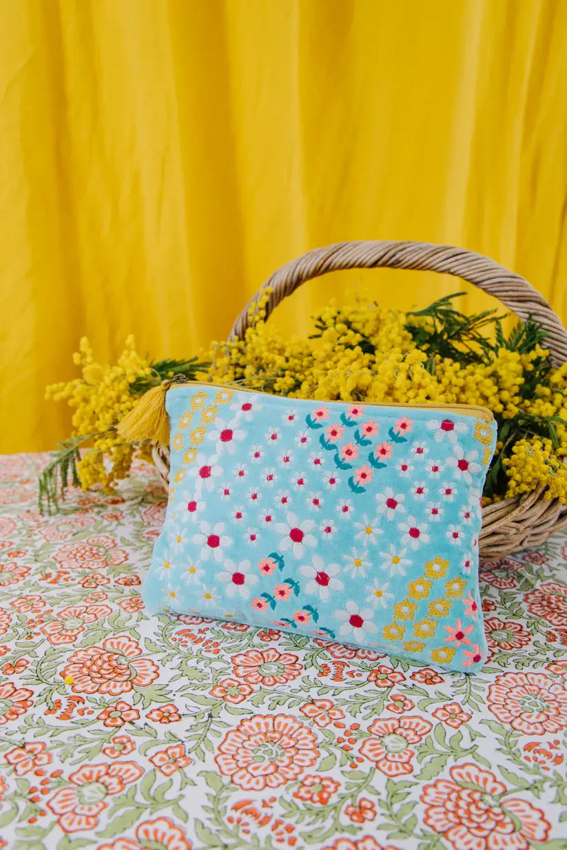 medium size pouch in pale blue velvet type material with white with red centres yellow and  pink flowers embroidered on the front with mustard coloured zip and tassel on the end.