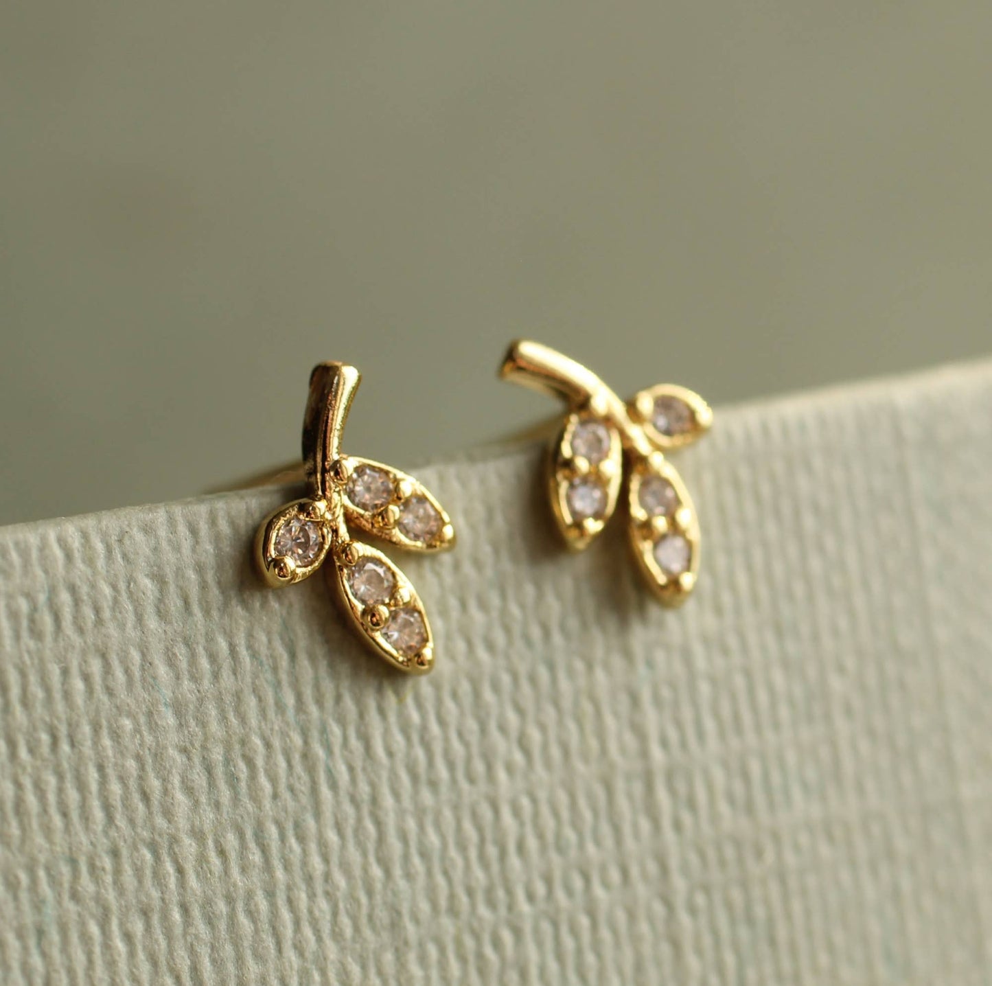 close up image of a pair of gold earrings in a leaf design. each earring has 3 gold leaves with one leaf set with one crystal and the other 2 leaves are set with 2 crystals.