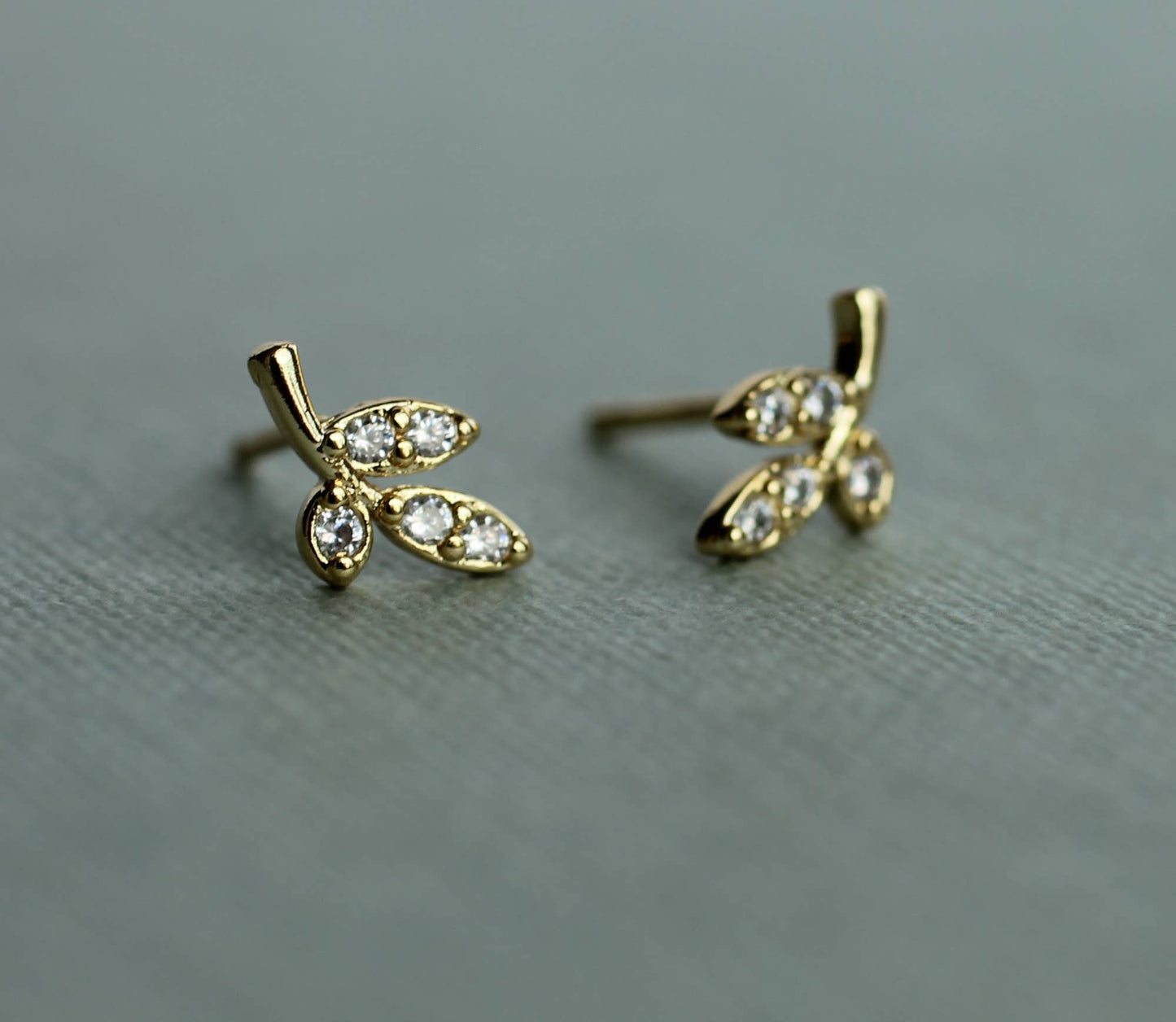 close up image of a pair of gold earrings in a leaf design. each earring has 3 gold leaves with one leaf set with one crystal and the other 2 leaves are set with 2 crystals.