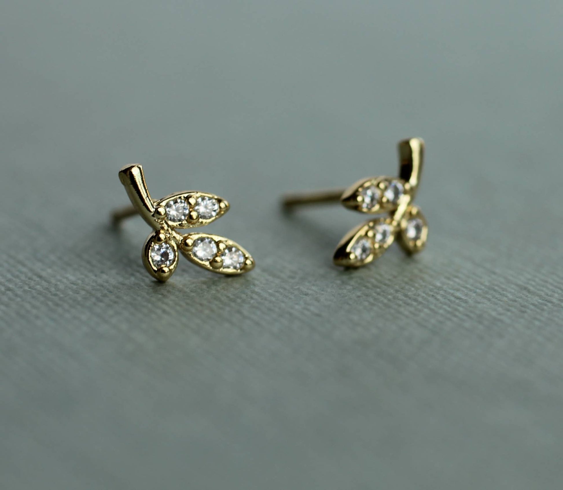 close up image of a pair of gold earrings in a leaf design. each earring has 3 gold leaves with one leaf set with one crystal and the other 2 leaves are set with 2 crystals.