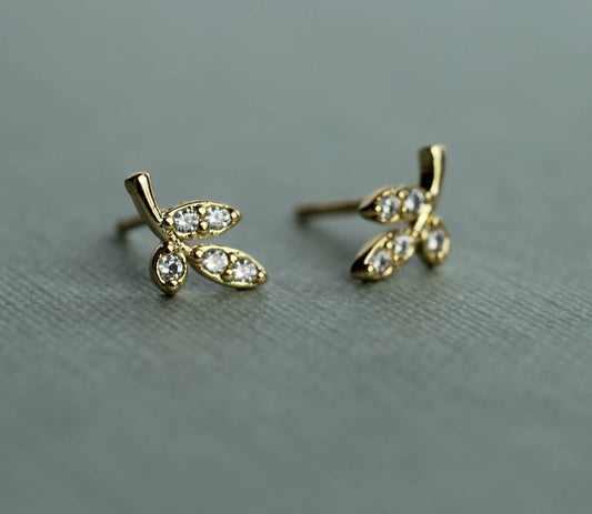 close up image of a pair of gold earrings in a leaf design. each earring has 3 gold leaves with one leaf set with one crystal and the other 2 leaves are set with 2 crystals.