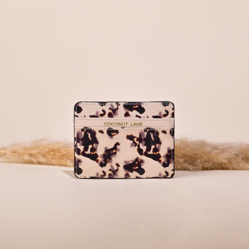 image of a card wallet with 2 sections. the middle section has the word coconut lane embossed in gold foil on it. the print is similar to an ink blot design with the base colour being a pale ivory colour with dark brown ink blots