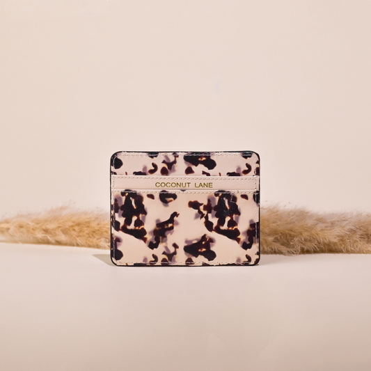 image of a card wallet with 2 sections. the middle section has the word coconut lane embossed in gold foil on it. the print is similar to an ink blot design with the base colour being a pale ivory colour with dark brown ink blots