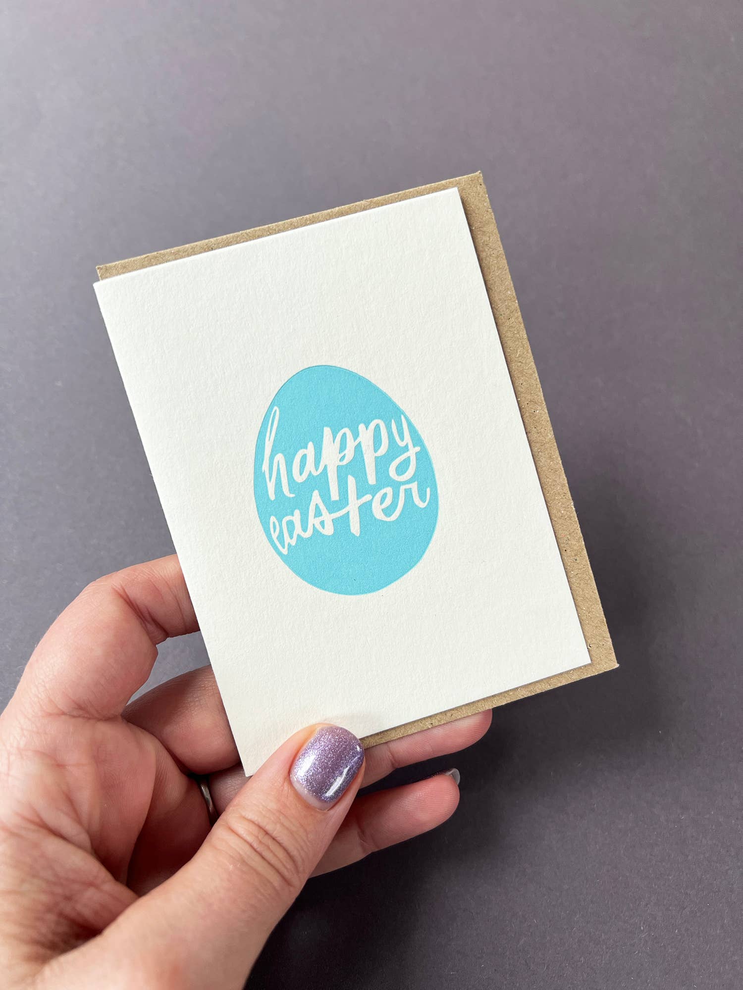 Hand holding a card with 'Happy Easter' on a gray background