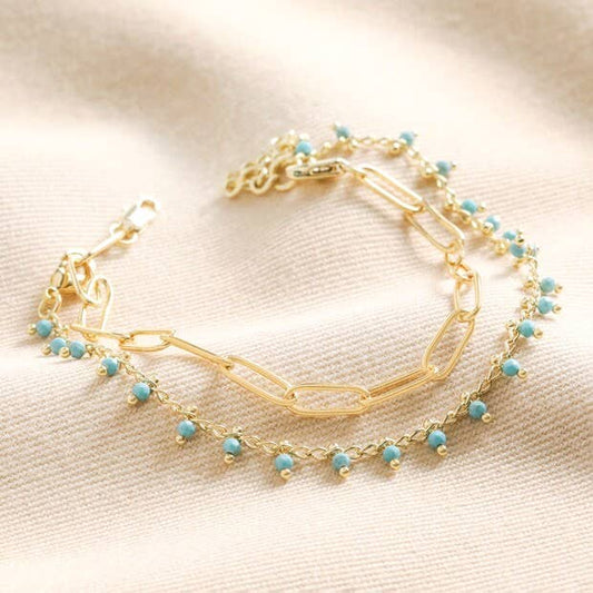 Gold chain link bracelet with a separate row of turquoise beads on a beige fabric background