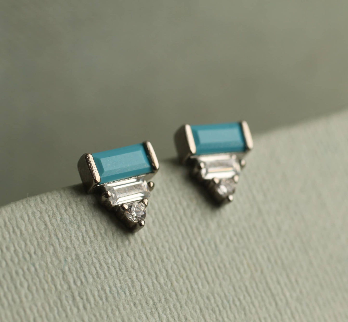 close up image of a pair of art deco earrings with  a turquoise rectangular stone and set underneath are to crystal stones. the earrings are set within silver