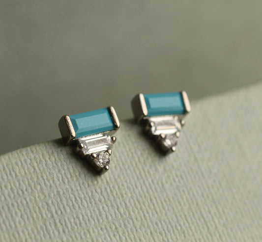 close up image of a pair of art deco earrings with  a turquoise rectangular stone and set underneath are to crystal stones. the earrings are set within silver