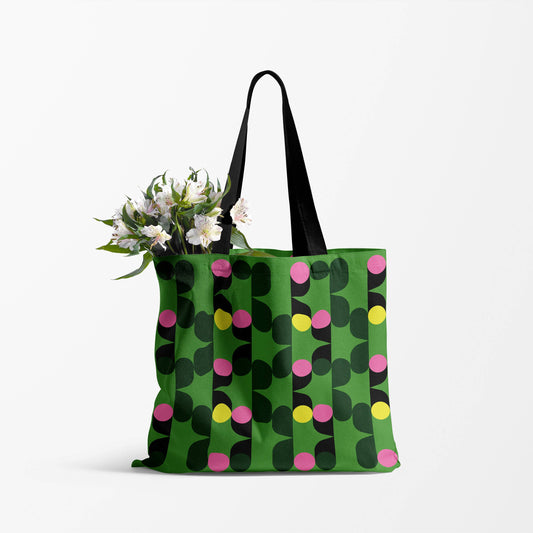 image shows a green tote bag with black handles and a viabrant design of pink, yellow and black circles. 