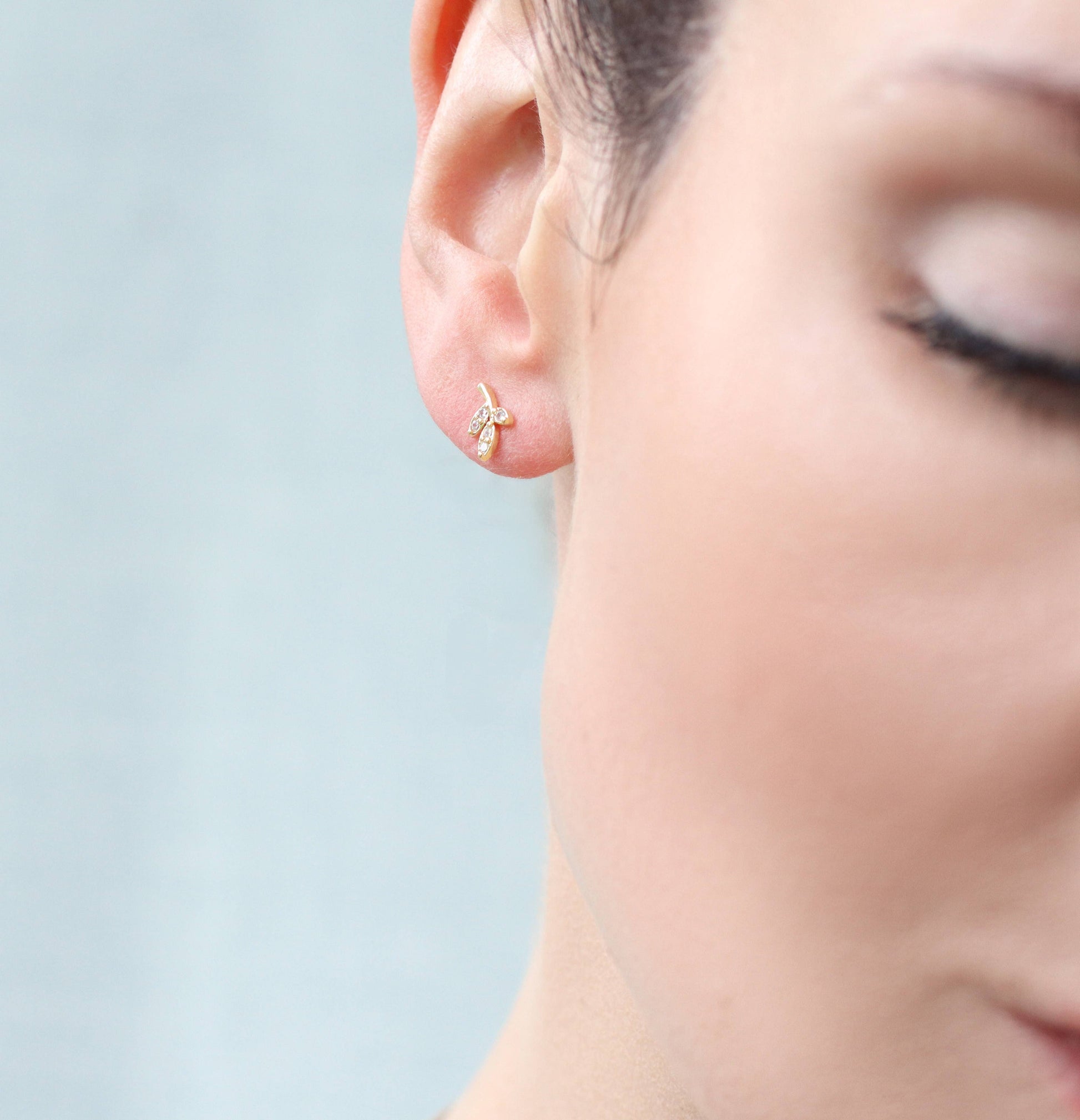 close up image a  lady wearing one earring with a design of 3 small crystal leafs with gold surround