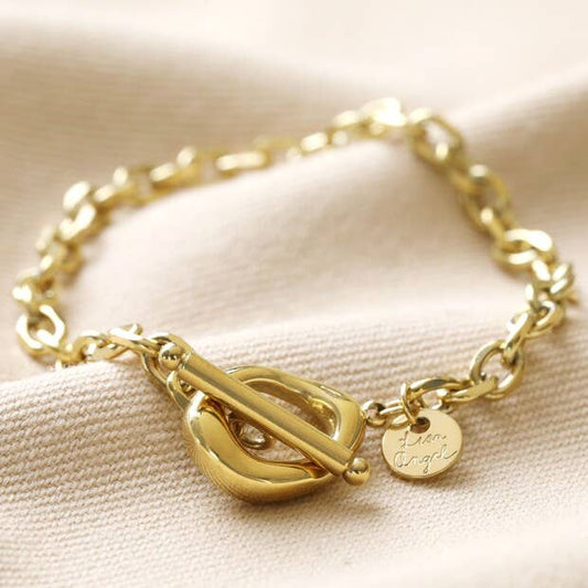 Gold bracelet with a unique clasp design on a beige fabric background