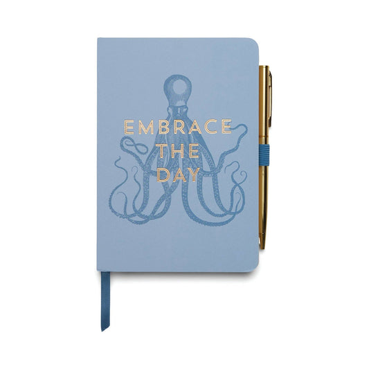 image shows a pale blue a5 notebook with  an image of a octopus drawn in a darker blue colour at the centre. across the middle of the octopus are the words Embrace the day in gold foil. to the right handside of the notebook is a blue elastic loop with gold ball point pen.