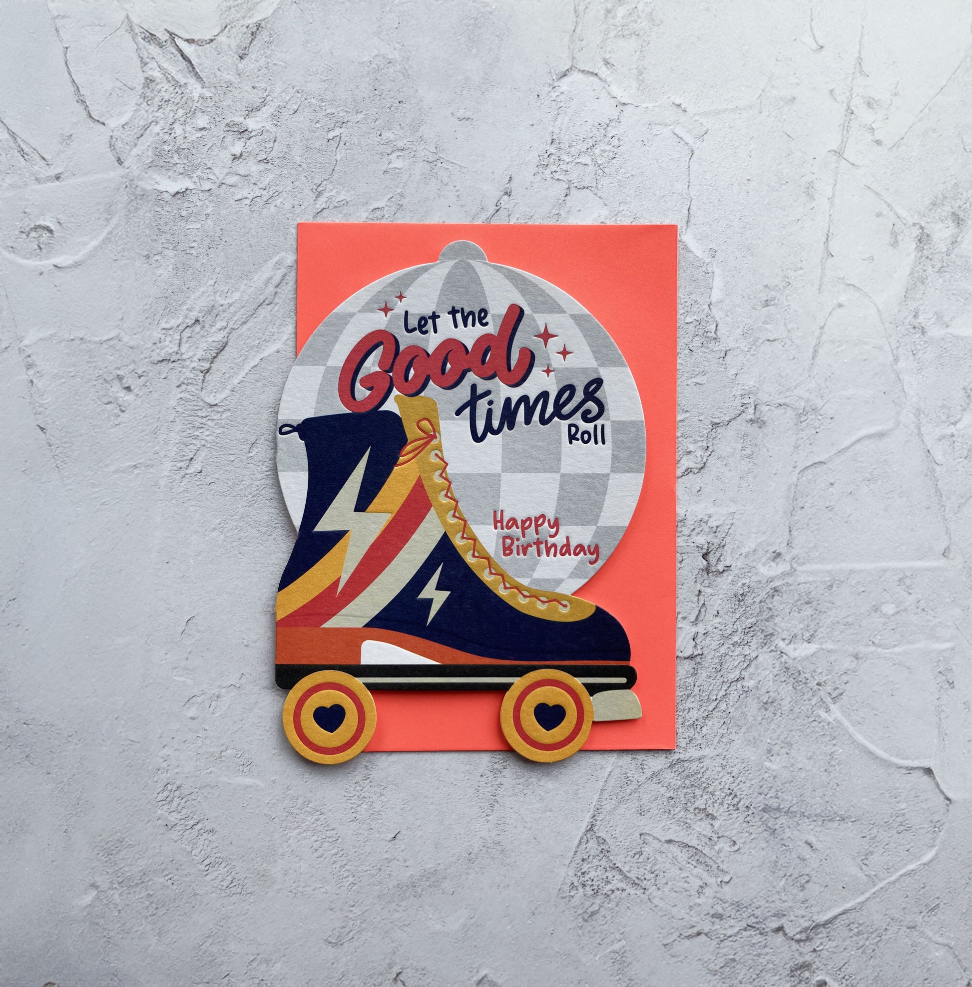 Roller derby boot with 'Let the Good Times Roll' text on a red card against a gray textured background
