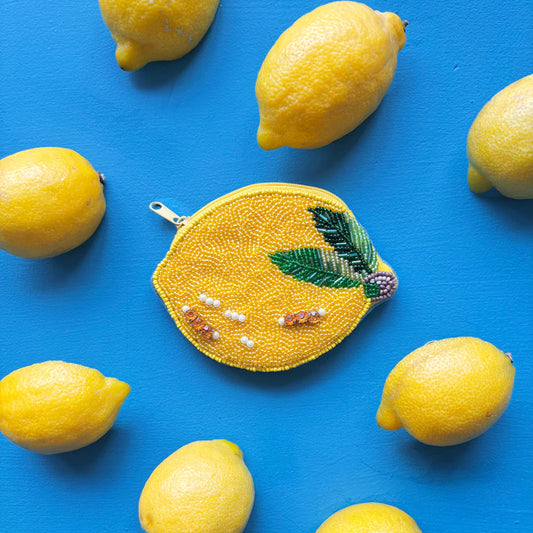 Decorative lemon-shaped pouch with bead details on a blue background with real lemons.