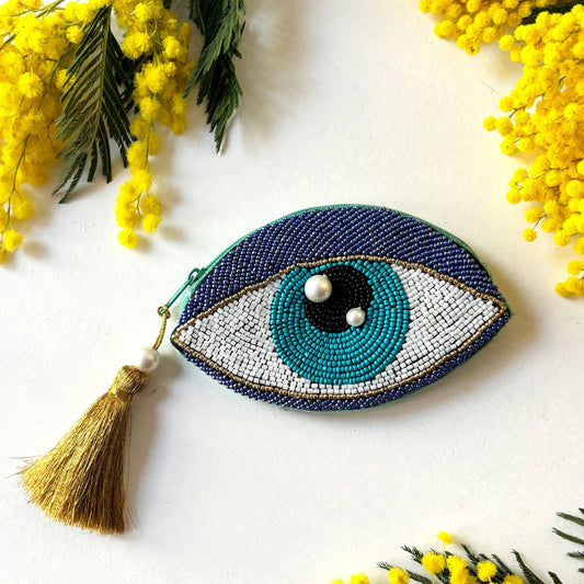 Beaded eye-shaped decorative item with a tassel on a white background with yellow flowers.