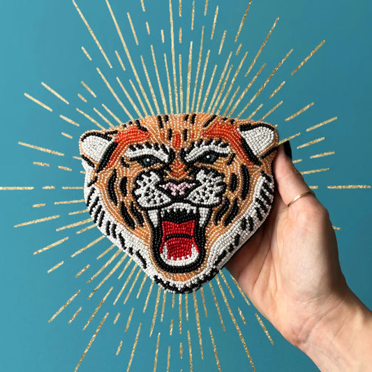Hand holding a beaded tiger head purse against a blue background with gold accents