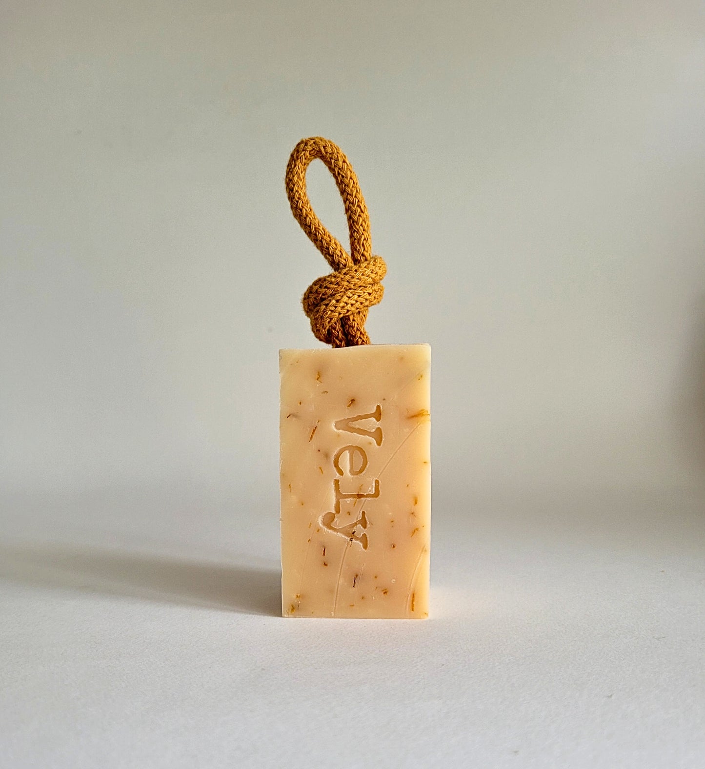 cream soap bar with dark orange rope and the word Vely etched into the soap.