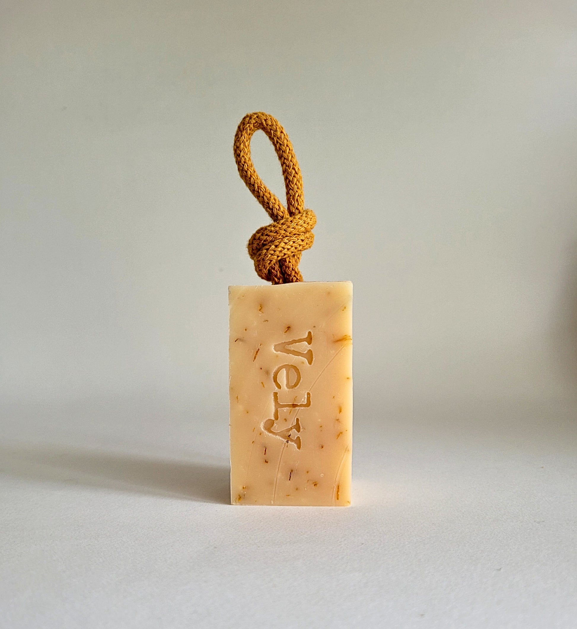 cream soap bar with dark orange rope and the word Vely etched into the soap.