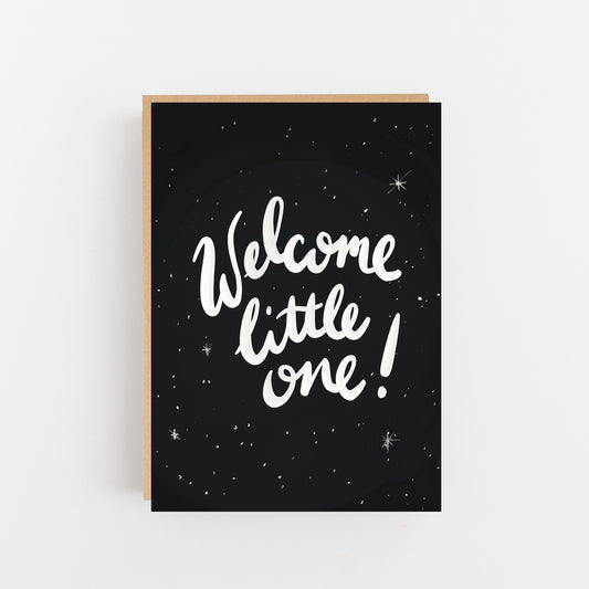 Greeting Card with Black background with wite small spots and stars. The words Welcome little one! written in white on the centre of the card. Brown Kraft Envelope