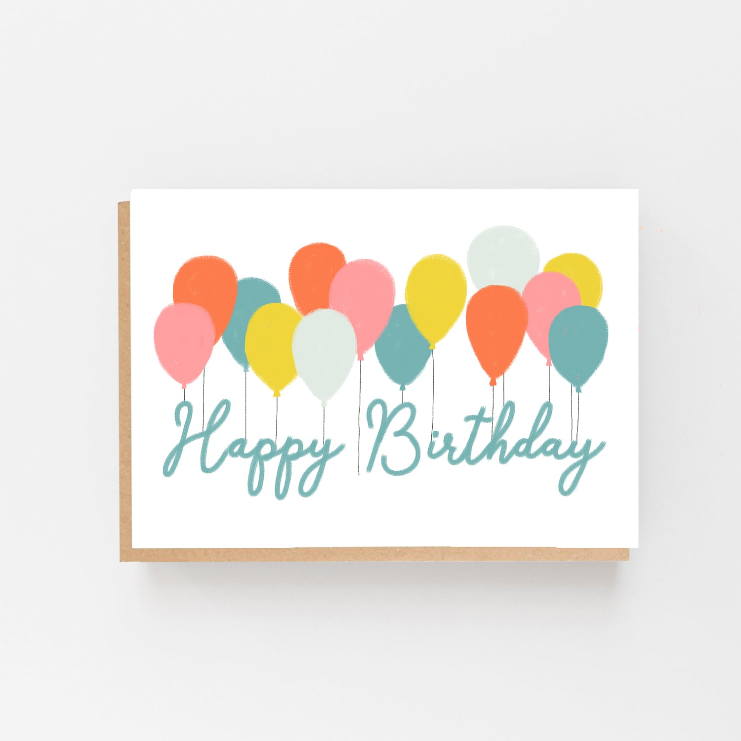 Greetings card in landscape.White Background with a row of pastel coloured balloons all across the centre of the card. With the words Happy Birthday in pale blue italics. Brown Kraft Envelope.