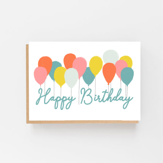 Greetings card in landscape.White Background with a row of pastel coloured balloons all across the centre of the card. With the words Happy Birthday in pale blue italics. Brown Kraft Envelope.