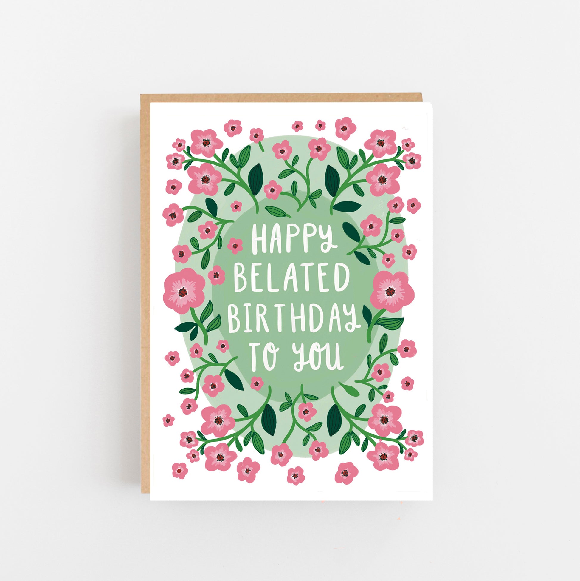 Greeting Card with the words Happy Belated Birthday to you written in White Capitals in the centre of the card on a pale blue background and surrounded by the drawings of pale pink and green flowers.