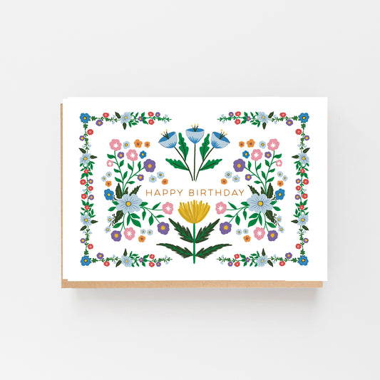 Greeting Card in landscape with a white background a drawing of dainty multi coloured flowers with the words Happy Birthday in the middle in Pink writing above and below the writing are larger flowers in blue and yellow. Brown Kraft Envelope.