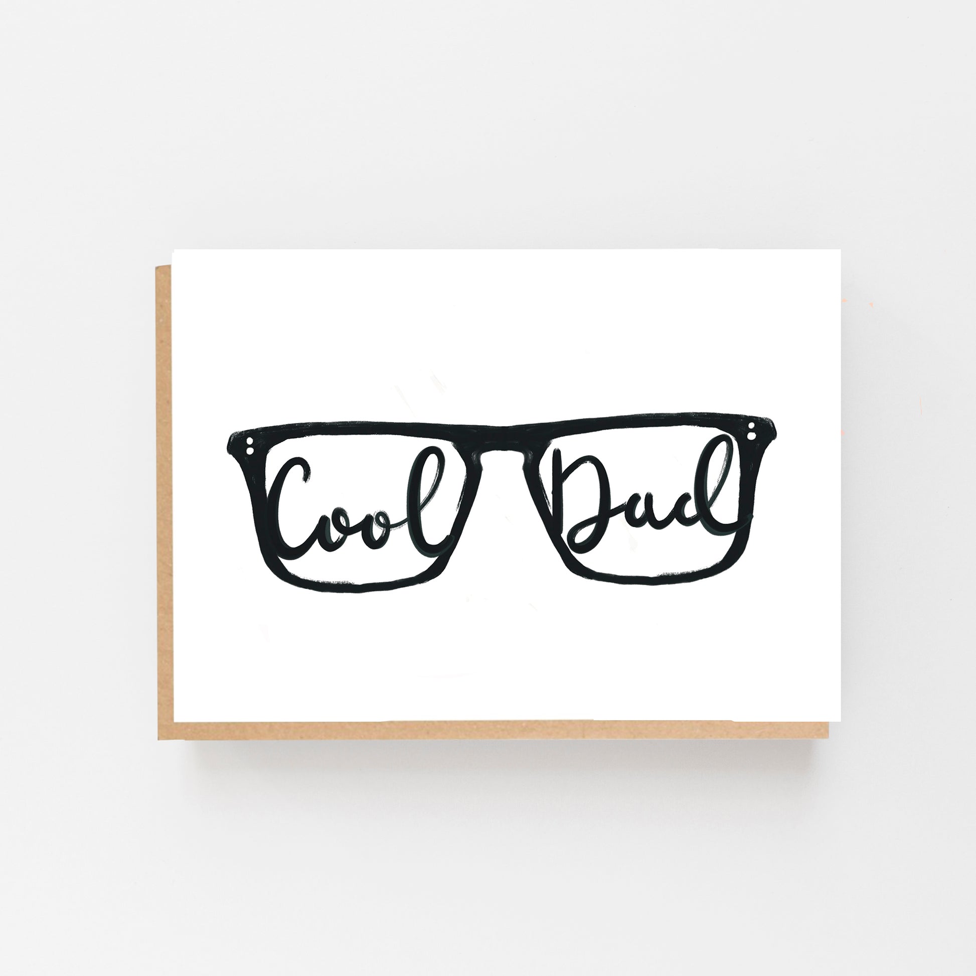 Greeting Card in landscape with the drawing of a pair of glasses in black on a white background with the words Cool in one lense and Dad in the other in Black Italic writing. Brown Kraft Envelope.