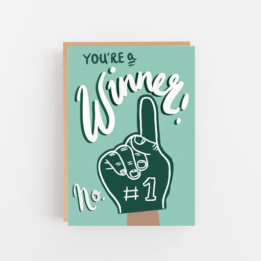 Greeting Card with a pale blue background in the centre a drawing of a hand in turquiose and white with a finger pointing to words at the top of the card that say You're a Winner in Italic writing in white and turquoise on the hand there is written # 1 and the word No in white to the left hand side of the hand. Brown Kraft Envelope