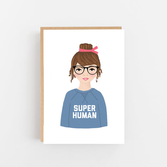 Greeting card with a white background with a drawing of a girl in the centre who has brown hair in a top knot with a pink ribbon. The girl has a pretty face wearing black glasses and has a pale blue jumper on with the words SUPER HUMAN in white writing. Brown Kraft Envelope