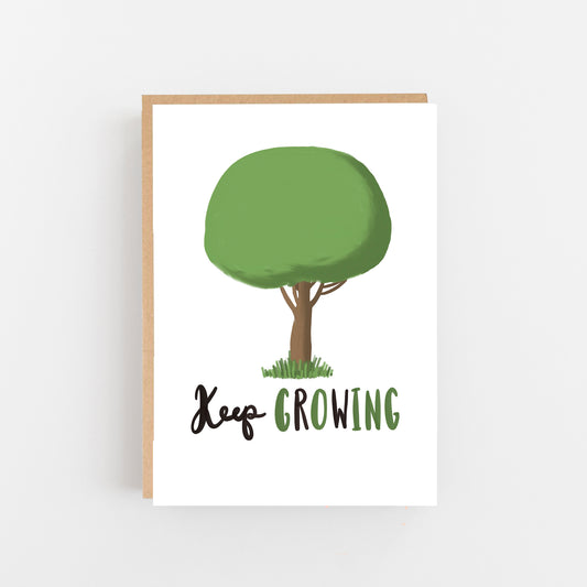 Greeting Card with a white backgroung in the cetre a drawing of a tree top of tree a green rounded shape. Brown tree trunk at the bottom green grass. under the tree the words Keep Growing written in black and green. Brown Kraft Envelope