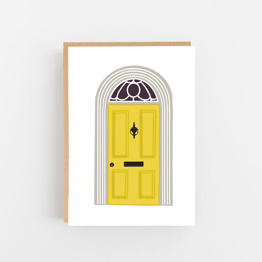 Greeting Card with a white background with the drawing of a front door on it . The door is old traditional style in yellow with a black door knocker and letterbox the door frae is white and grey with a rounded top and glass panel drawing above the front door. Brown Kraft Envelope
