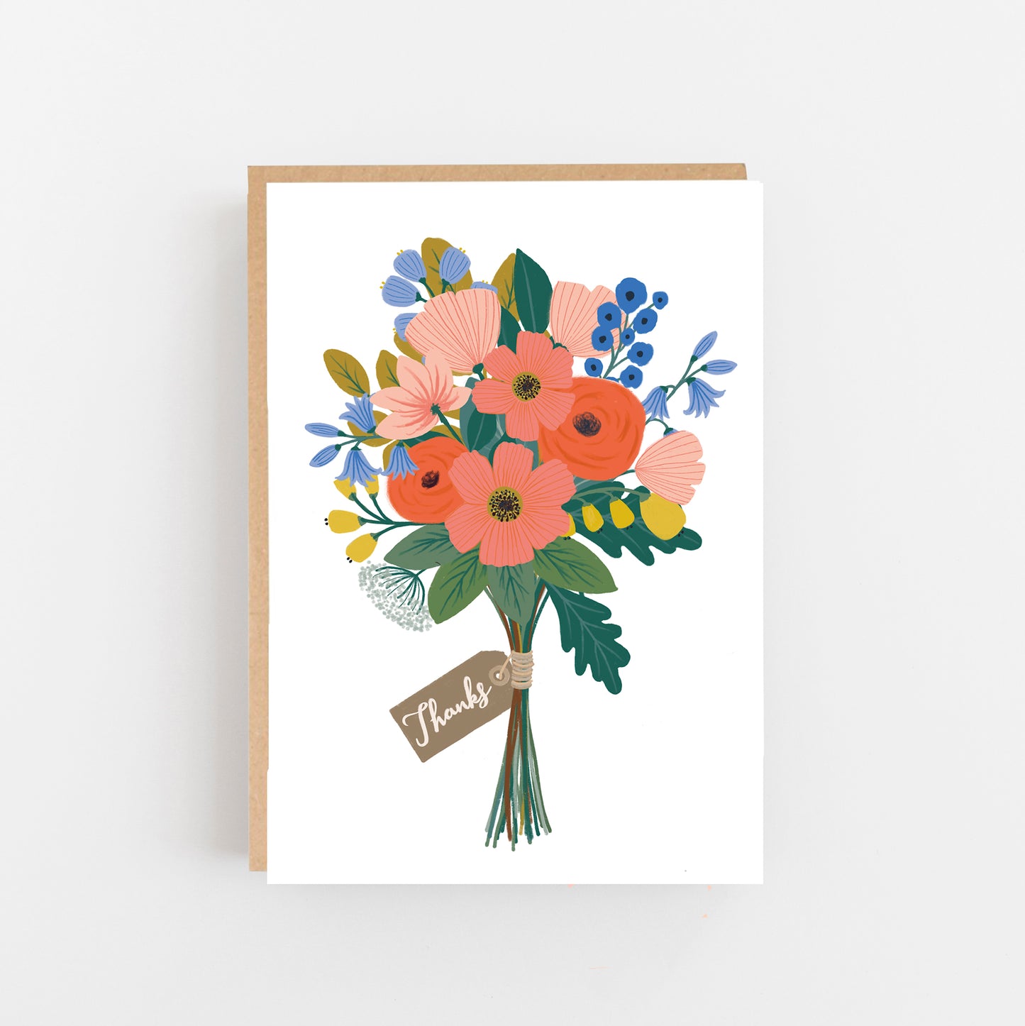 Greeting card with the word thanks in small italic writing in white on a grey gift tag wrapped around a bunch of multicoloured flowers in pins blue green and yellow on a white background. Brown Kraft envelope