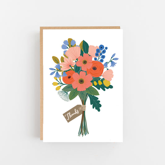 Greeting card with the word thanks in small italic writing in white on a grey gift tag wrapped around a bunch of multicoloured flowers in pins blue green and yellow on a white background. Brown Kraft envelope