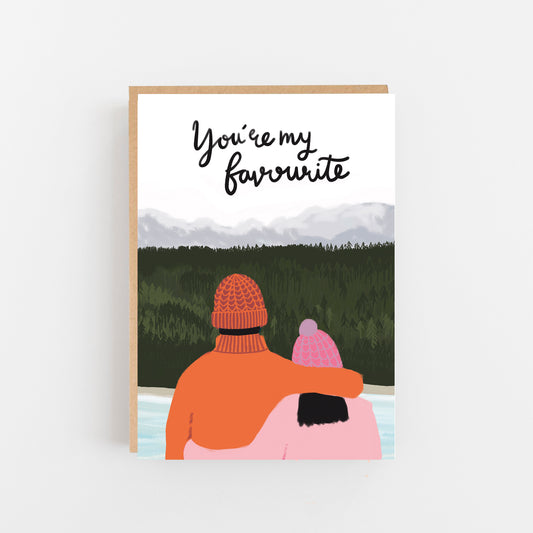 Greeting Card with the words You're my favourite in black italic writing on the top of the card below a picture of a forest with green tress and in front of this the back of a man and a lady both wearing bobble hats the man in an orange jumper and hat the lady in pale pink hat and jumper. Brown Kraft  envelope.